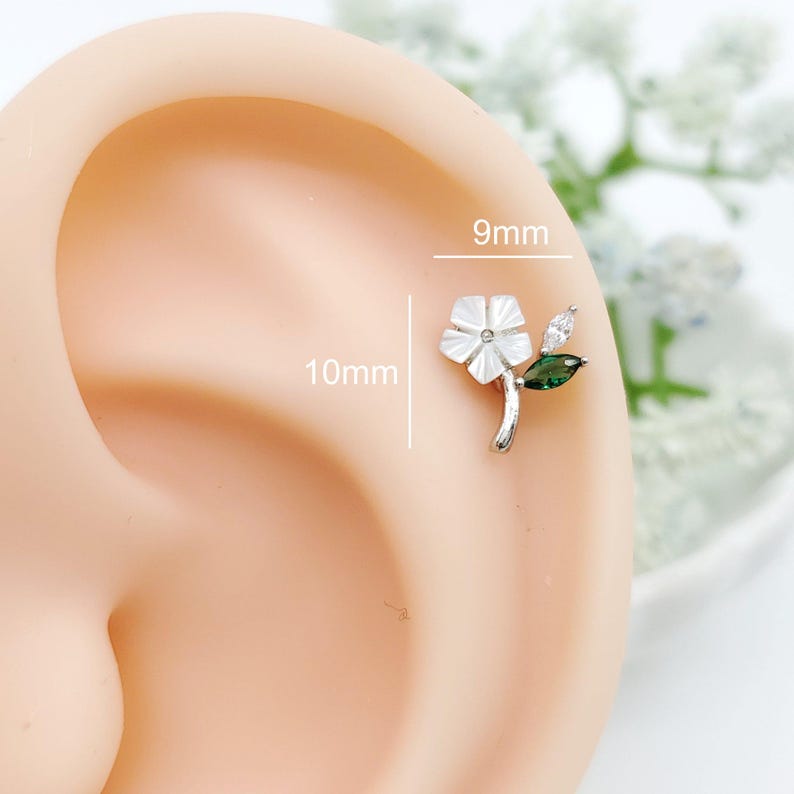 May include: A silver-toned flower earring stud featuring a white petal design, a clear marquise-cut stone, and a green marquise-cut stone. The earring measures 9mm in width and 10mm in height, as indicated by the text labels on the image.