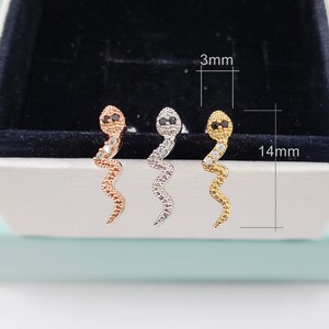 May include: Three snake-shaped earrings with black eyes and clear rhinestones. The earrings are 14 mm long and 3 mm wide. The earrings are available in gold, silver, and rose gold.