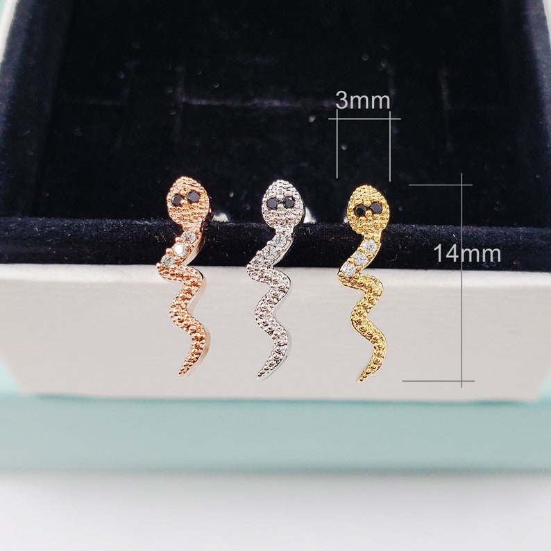 May include: Three snake-shaped earrings with black eyes and clear rhinestones. The earrings are 14 mm long and 3 mm wide. The earrings are available in gold, silver, and rose gold.