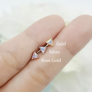 May include: Three triangle-shaped earrings with clear stones, shown in gold, silver, and rose gold.