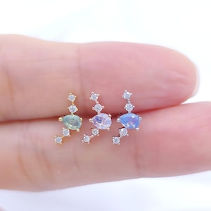 Op de afbeelding: Drie oorstekers met een hemels ontwerp. Elke oorbel heeft een druppelvormige edelsteen in groen, lavendel en blauw, geaccentueerd met kleine, sprankelende, heldere stenen. De oorbellen worden gepresenteerd tegen een witte achtergrond.