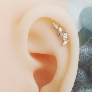 May include: A silver ear piercing with a row of clear marquise-shaped stones set in a leaf design.