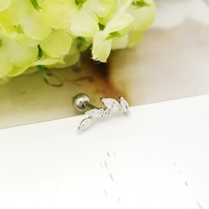 May include: A silver body piercing with a small ball at the top and a curved line of clear cubic zirconia stones.