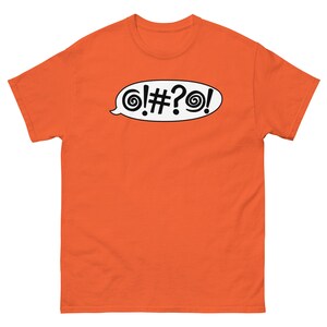 May include: Orange t-shirt with a white speech bubble containing the text "! # ? !" and a swirl design on each side.