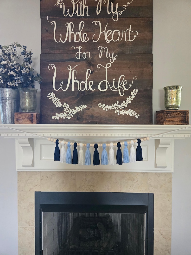 Tassel garland with navy, Carolina blue, and white yarn tassels on wood beads, styled on a white fireplace mantel – North Carolina dorm decor, graduation party banner, handmade college room decoration