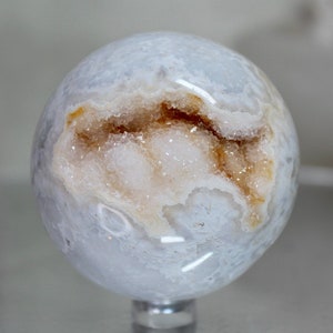 May include: A white agate sphere with a natural geode opening revealing a crystal cluster with brown and white accents.