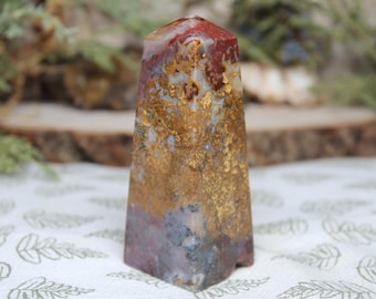 May include: A red, white, and gold agate crystal point. The crystal is polished and has a smooth, shiny surface. The point is about 2 inches tall.