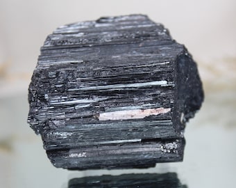 May include: A large, black, rough, and raw piece of black tourmaline crystal. The crystal has a striated, layered appearance.