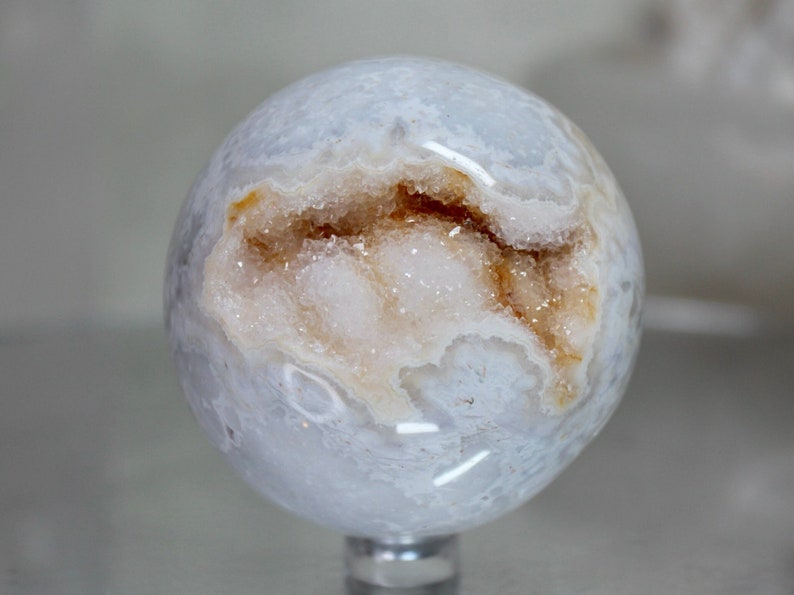 May include: A white agate sphere with a natural geode opening revealing a crystal cluster with brown and white accents.