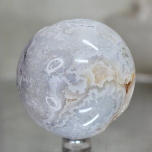 May include: A white agate sphere with a swirling pattern of white and light grey. The sphere is polished and has a smooth surface.
