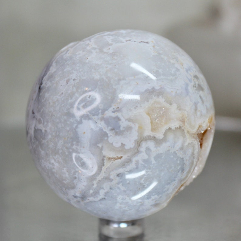 May include: A white agate sphere with a swirling pattern of white and light grey. The sphere is polished and has a smooth surface.