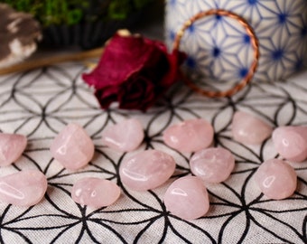 May include: A collection of ten pink rose quartz tumbled stones on a white and black patterned surface.