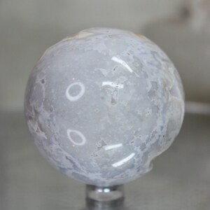 May include: A smooth, white agate sphere with a cloudy, marbled pattern. The sphere is polished and has a high gloss finish.