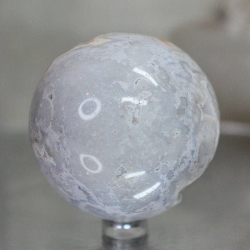 May include: A smooth, white agate sphere with a cloudy, marbled pattern. The sphere is polished and has a high gloss finish.