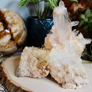 May include: A large cluster of clear quartz crystals with a white, milky base. The crystals are arranged in a cluster, with some pointing upwards and others pointing downwards. The base of the cluster is rough and textured, and the crystals are clear and sparkling.