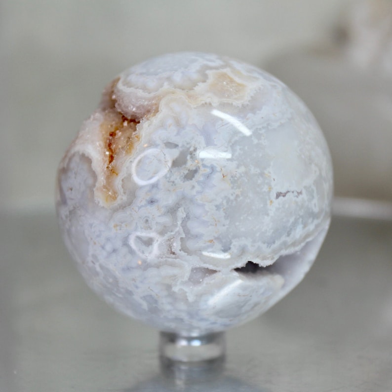 May include: A white agate sphere with brown and white banding and a crystal-like texture. The sphere is on a clear stand.