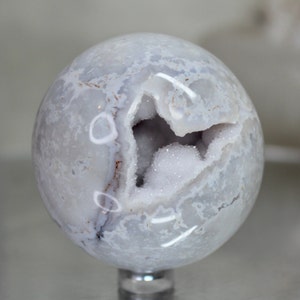 May include: A white agate sphere with a large, open geode cavity. The geode is lined with sparkling white crystals. The sphere is polished and has a smooth, glassy finish.
