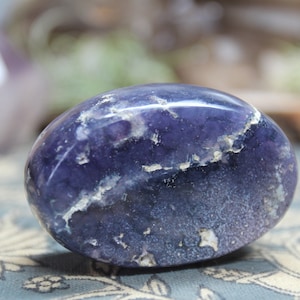 May include: A smooth, oval-shaped purple amethyst stone with white and gray swirls and markings.