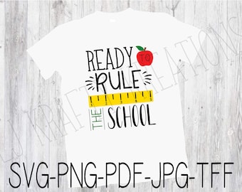 Może przedstawiać: Biała koszulka z czarnym napisem "Ready to Rule the School" z czerwonym jabłkiem i żółtą linijką.