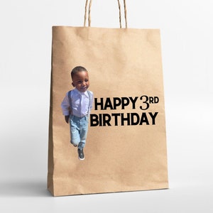 K&ouml;nnte beinhalten: Eine braune Papiert&uuml;te mit einem Foto eines kleinen Jungen und dem Text "HAPPY 3RD BIRTHDAY" auf der Vorderseite.