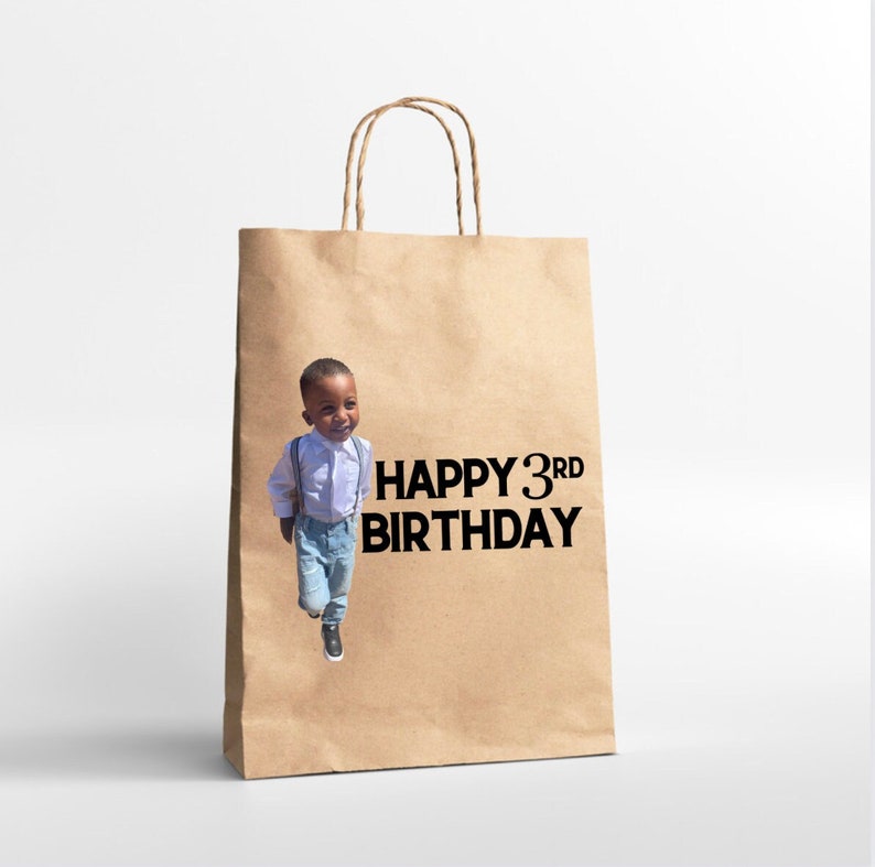 K&ouml;nnte beinhalten: Eine braune Papiert&uuml;te mit einem Foto eines kleinen Jungen und dem Text "HAPPY 3RD BIRTHDAY" auf der Vorderseite.