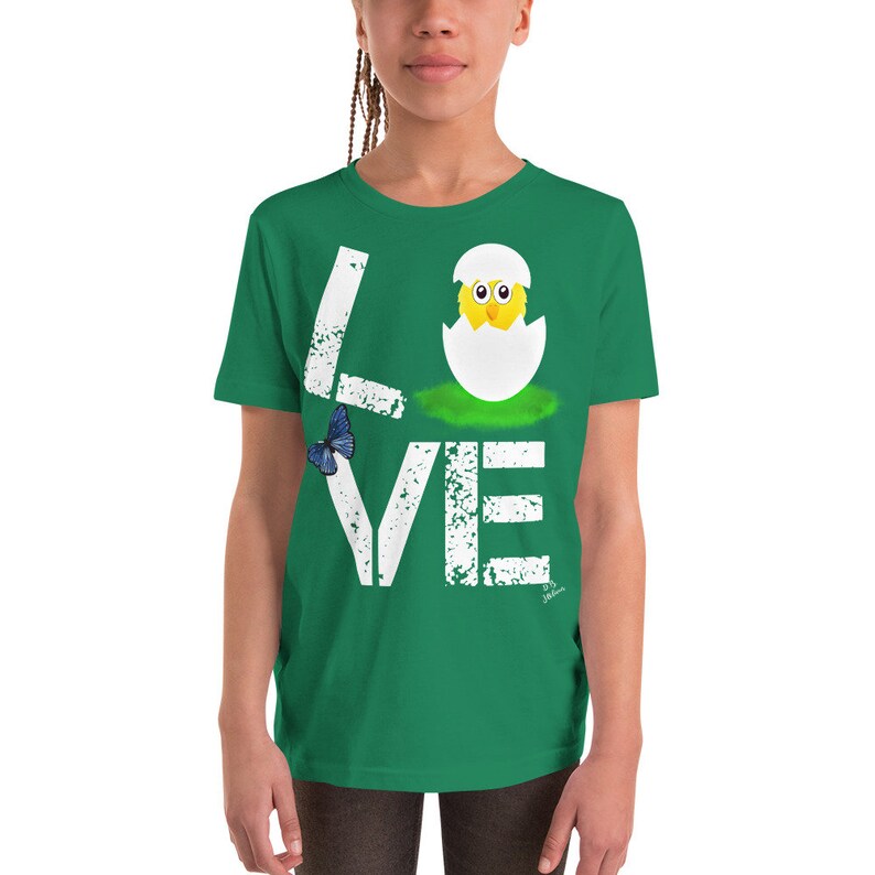 K&ouml;nnte beinhalten: Ein gr&uuml;nes T-Shirt f&uuml;r Jugendliche mit einer wei&szlig;en, abgenutzten Grafik, auf der "LOVE" steht, wobei ein K&uuml;ken in der Mitte des Wortes aus einem Ei schl&uuml;pft. Links neben dem Wort befindet sich ein blauer Schmetterling.