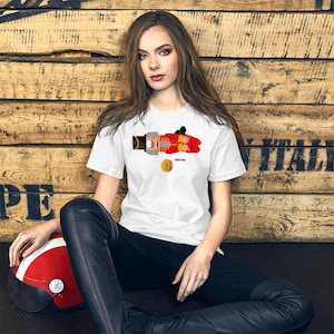 Könnte beinhalten: Weißes T-Shirt mit einem Aufdruck eines Nussknackers und einer Walnuss. Der Nussknacker trägt ein rot-schwarzes Kostüm und hält ein Schwert. Die Walnuss ist braun mit einer hellbraunen Schale.