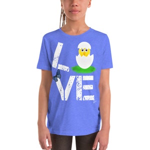 K&ouml;nnte beinhalten: Ein blaues T-Shirt f&uuml;r Jugendliche mit einer wei&szlig;en, abgenutzten Grafik, auf der "LOVE" steht, wobei ein K&uuml;ken aus einem Ei im "O" schl&uuml;pft.