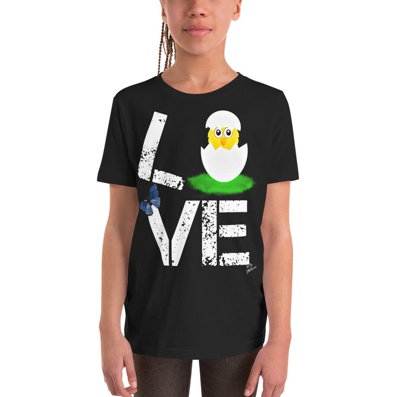 K&ouml;nnte beinhalten: Schwarzes T-Shirt f&uuml;r Jugendliche mit einem wei&szlig;en, abgenutzten Aufdruck, der "LOVE" sagt, mit einem K&uuml;ken, das aus einem Ei im "O" schl&uuml;pft. Ein blauer Schmetterling befindet sich neben dem "L".