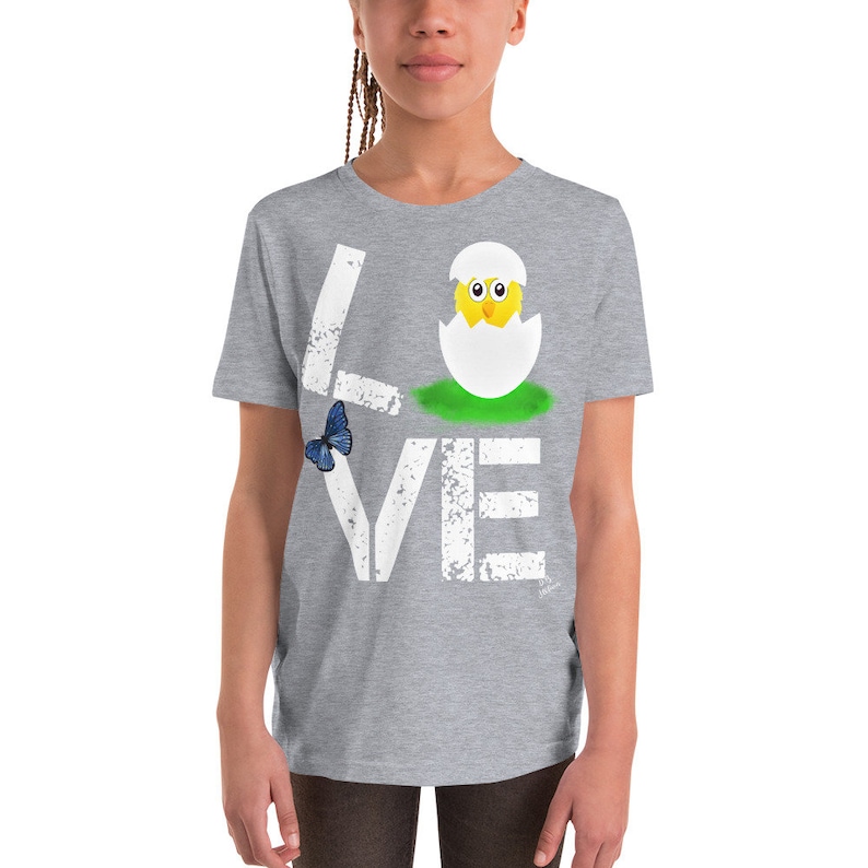 K&ouml;nnte beinhalten: Ein graues T-Shirt f&uuml;r Jugendliche mit einer wei&szlig;en, abgenutzten Grafik, auf der "LOVE" steht, wobei ein K&uuml;ken in der Mitte des Wortes aus einem Ei schl&uuml;pft. Links neben dem Wort befindet sich ein blauer Schmetterling.