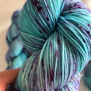 May include: Teal and purple yarn with flecks of colour. The yarn is soft and fluffy, and it is perfect for knitting or crocheting.