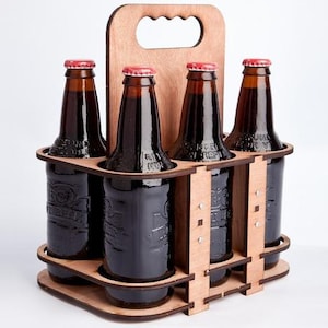 May include: Wooden six-pack bottle carrier with a handle. The carrier is made of light brown wood and has a natural finish. It holds six bottles of dark brown liquid.