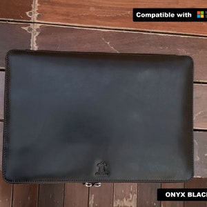 Może przedstawiać: Czarna skórzana torba na laptopa z zamkiem błyskawicznym. Torba jest kompatybilna z urządzeniami Microsoft Surface. Tekst "ONYX BLACK" jest nadrukowany na dole obrazu.