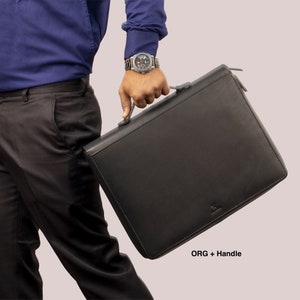 May include: A black leather briefcase with a handle and a zipper. The briefcase is being held by a person wearing a blue shirt and black pants.