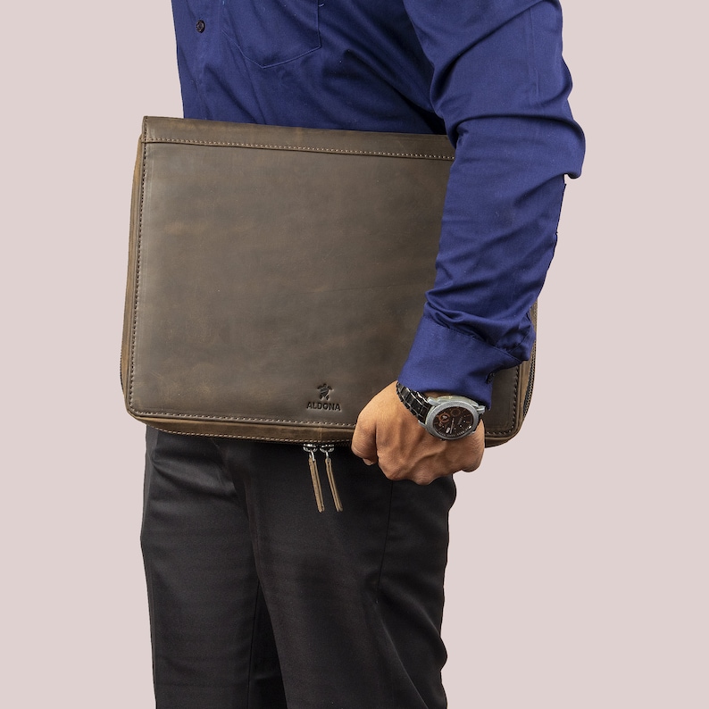 May include: A brown leather portfolio with a zipper closure and a small logo that says "Aldona".