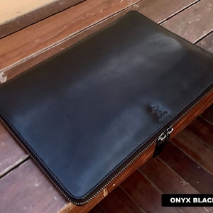 May include: A black leather laptop sleeve with a zipper closure. The sleeve has a subtle embossed logo on the front. The text "ONYX BLACK" is visible in the bottom right corner of the image.
