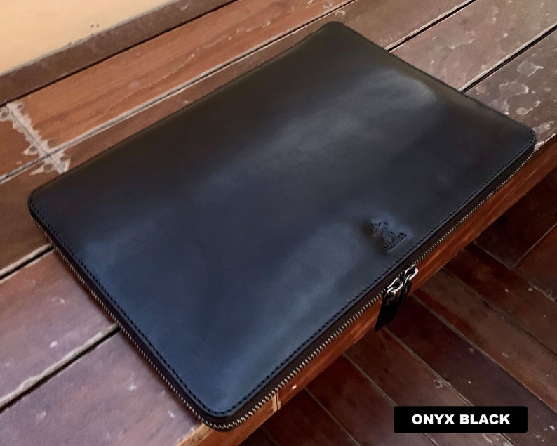 May include: A black leather laptop sleeve with a zipper closure. The sleeve has a subtle embossed logo on the front. The text "ONYX BLACK" is visible in the bottom right corner of the image.