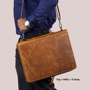 May include: A brown leather briefcase with a zipper closure and a shoulder strap. The briefcase has a handle and a small logo on the front. Org + HNDL + S Strap