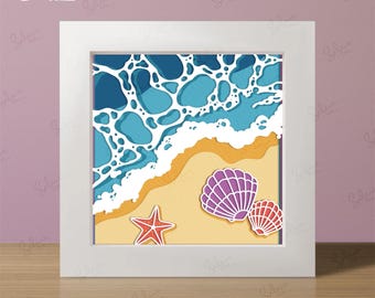 May include: A framed paper art piece depicting a beach scene with layered blue waves, tan sand, a red starfish, and two seashells. The frame is white, and the text "DIGITAL DOWNLOAD" is visible. The bottom of the frame reads "+Free Frame" and "SVG • DXF • PDF • PNG".