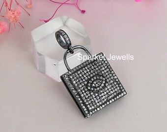 May include: A black pendant in the shape of a handbag, encrusted with small, sparkling stones. The pendant has a silver-colored handle and a ring at the top. The text "Sparkel Jewells" is visible on the side.