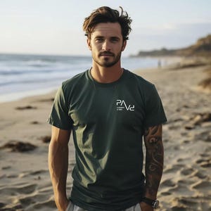 K&ouml;nnte beinhalten: Dunkelgr&uuml;nes T-Shirt mit dem wei&szlig;en Text "PAVd CLEMENT & SONS" auf der Brust. Das Shirt ist kurz&auml;rmlig und hat einen Rundhalsausschnitt. Das Bild ist an einem Strand mit dem Meer im Hintergrund aufgenommen.