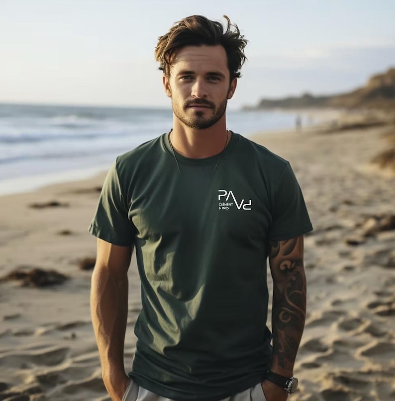 K&ouml;nnte beinhalten: Dunkelgr&uuml;nes T-Shirt mit dem wei&szlig;en Text "PAVd CLEMENT & SONS" auf der Brust. Das Shirt ist kurz&auml;rmlig und hat einen Rundhalsausschnitt. Das Bild ist an einem Strand mit dem Meer im Hintergrund aufgenommen.