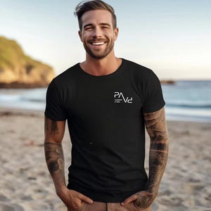 K&ouml;nnte beinhalten: Schwarzes T-Shirt mit Rundhalsausschnitt und dem wei&szlig;en Text "PAVe Clement & Ines" auf der Brust. Das Shirt ist kurz&auml;rmlig und aus einem weichen Material. Die Person steht an einem Sandstrand.
