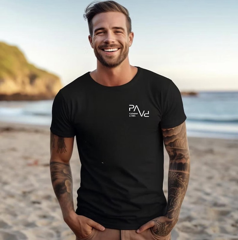K&ouml;nnte beinhalten: Schwarzes T-Shirt mit Rundhalsausschnitt und dem wei&szlig;en Text "PAVe Clement & Ines" auf der Brust. Das Shirt ist kurz&auml;rmlig und aus einem weichen Material. Die Person steht an einem Sandstrand.