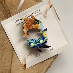 May include: Two wooden whale-shaped ornaments painted with famous artwork. One whale is painted with sunflowers and the other with a starry night sky. The ornaments are on a wooden surface with the text "ART WOOD HOUSE handmade wooden accessories @art_wood_house_"