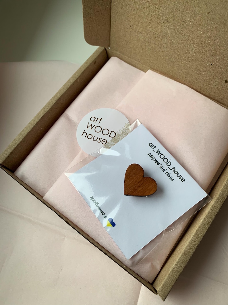 May include: A small wooden heart-shaped ornament in a clear plastic bag with a white card that says "art_WOOD_house Деревяні піні" and a sticker that says "art WOOD house".