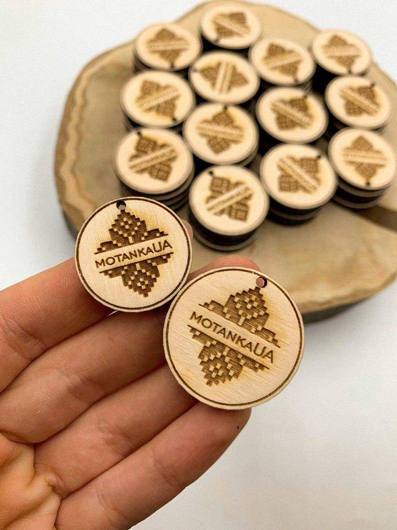 May include: Two wooden round tags with the text "MOTANKAUJA" and a geometric design. The tags are brown and have a hole at the top.