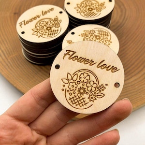 May include: A stack of round wooden tags with the text "Flower love" and a floral design. The tags have two holes for string or ribbon.