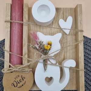 Könnte beinhalten: Ein dekoratives Holzstück mit einer weißen Katzen-Silhouette, einem weißen Kerzenhalter und einer bordeauxfarbenen Kerze. Die Katze hält einen kleinen Strauß Trockenblumen. Ein kleines Herz und ein Anhänger mit dem Text "FÜR Dich" sind ebenfalls enthalten.