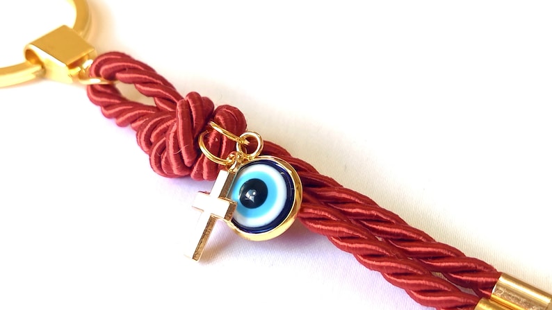 May include: Red braided rope keychain with a gold key ring, a gold cross charm, and a blue evil eye charm.